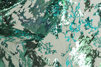 The image is a close-up of a fabric with a pattern of green and blue sequins, creating a visually striking and intricate design.