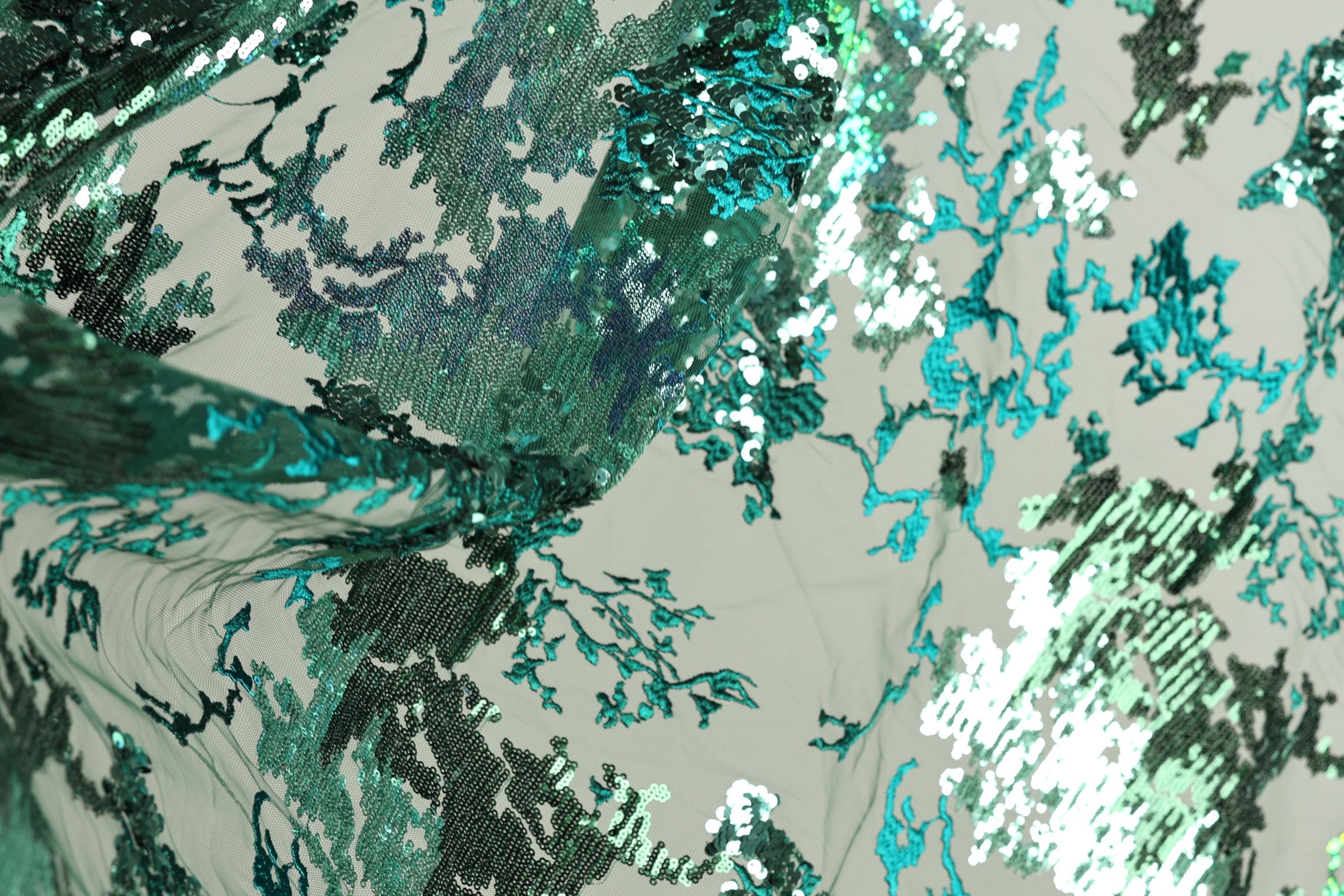 The image is a close-up of a fabric with a pattern of green and blue sequins, creating a visually striking and intricate design.