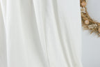 a white fabric, possibly a curtain or a sheer curtain, with a wreath of dried flowers or branches on the right side.