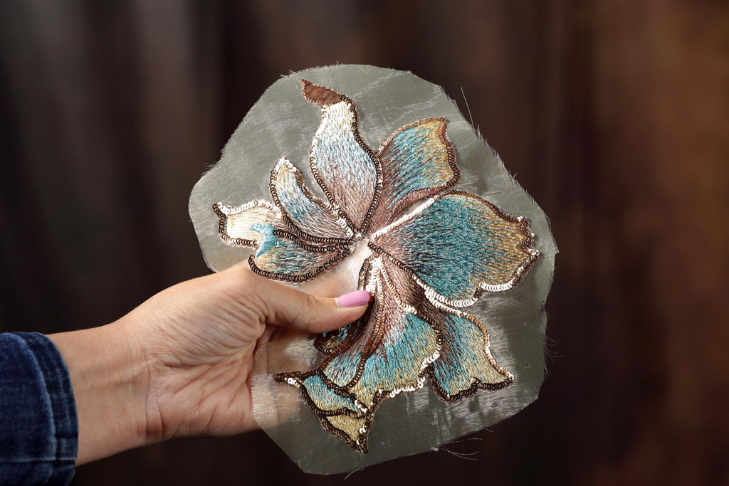 A hand holding a piece of fabric with a detailed embroidered flower design.