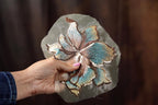 A hand holding a piece of fabric with a detailed embroidered flower design.