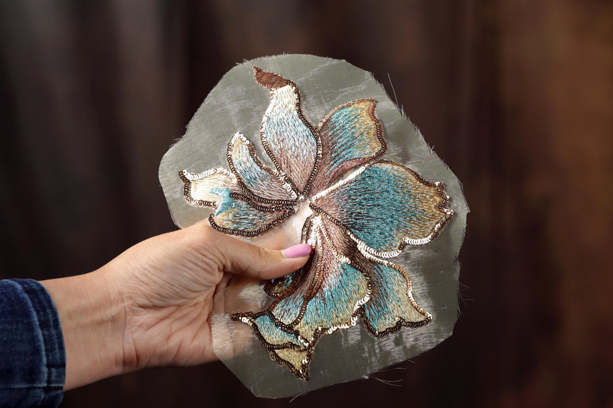 A hand holding a piece of fabric with a detailed embroidered flower design.