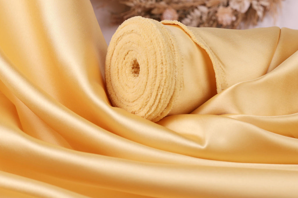 A close-up view of a yellow satin fabric, possibly silk, with a curled and folded appearance.