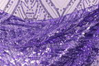 a close-up view of a fabric with a purple and white pattern, featuring a lot of small sequins or beads that create a sparkling, textured appearance.