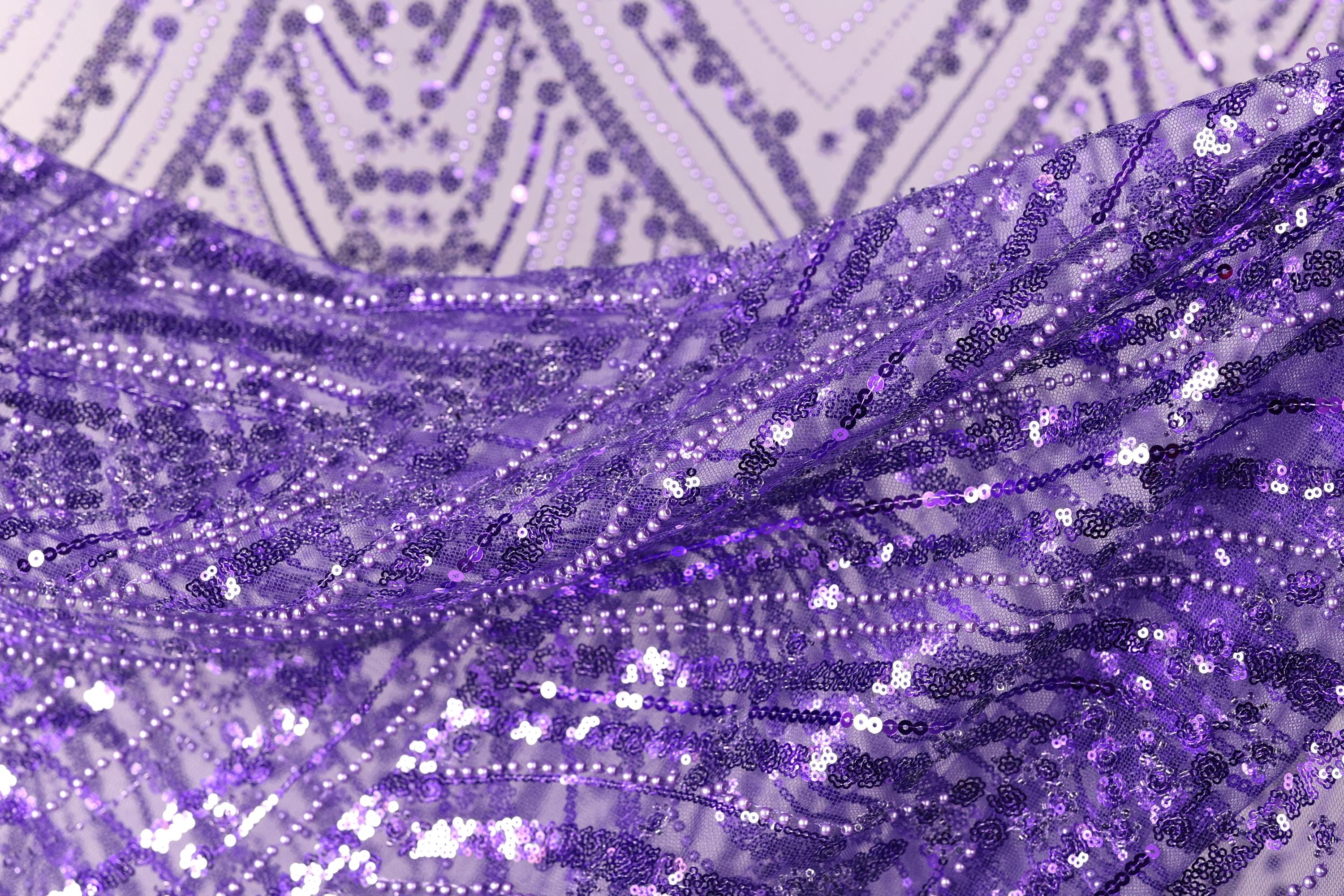 a close-up view of a fabric with a purple and white pattern, featuring a lot of small sequins or beads that create a sparkling, textured appearance.
