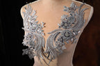 A mannequin wearing a dress with intricate silver and black embroidered details, including flowers and leaves, against a dark background.