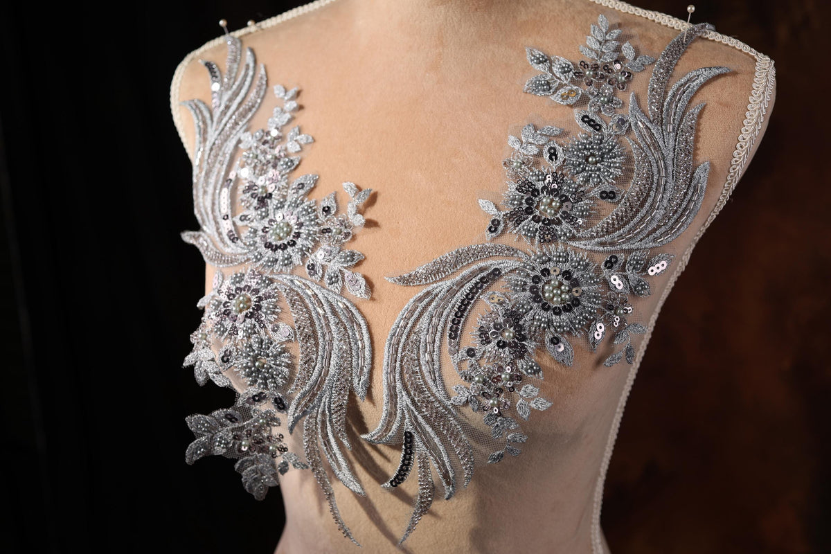 A mannequin wearing a dress with intricate silver and black embroidered details, including flowers and leaves, against a dark background.