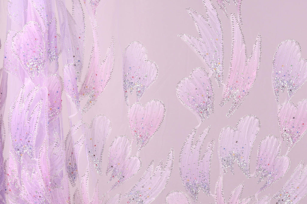 a close-up view of a fabric with a delicate, pastel-colored floral pattern. The fabric appears to be made of a sheer material, with a pink and purple color scheme. The pattern consists of numerous small, intricately designed flowers or leaves, each adorned with tiny glitter or sequin accents. The overall appearance of the fabric is soft and delicate, with a subtle, elegant aesthetic.