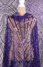 a mannequin wearing a purple sequin dress with a sheer overlay. The dress has a pattern of purple and black sequins, creating a visually striking and elegant design.