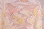 a close-up view of a delicate, intricately embroidered fabric with a floral pattern. The fabric is adorned with numerous small, sparkling beads that add a touch of elegance and sparkle to the design. The close-up perspective allows for a detailed examination of the fabric's texture and the intricate details of the embroidery.