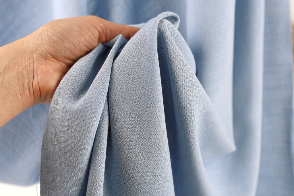 A hand is holding a folded light blue fabric, which appears to be a piece of clothing or textile.