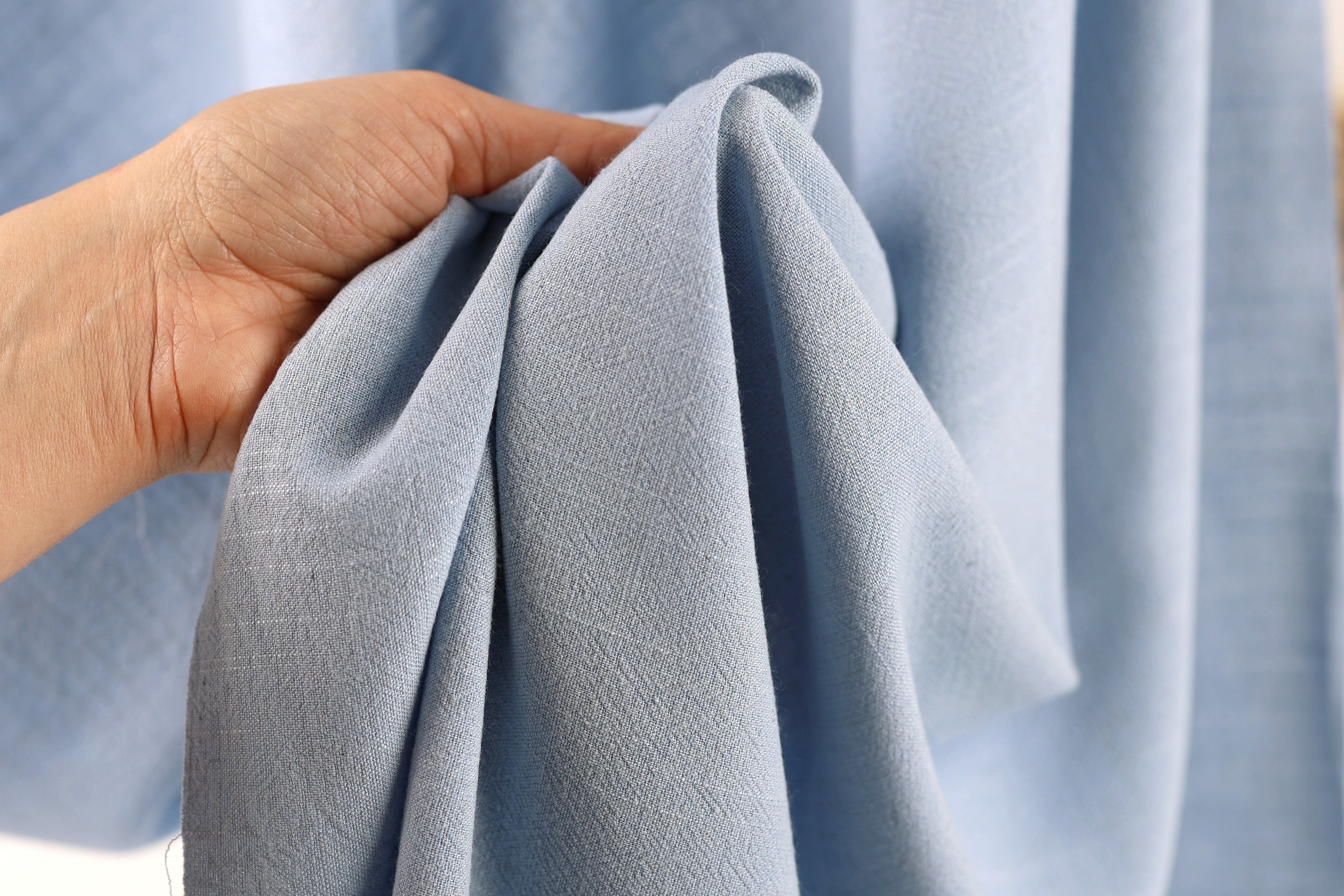 A hand is holding a folded light blue fabric, which appears to be a piece of clothing or textile.
