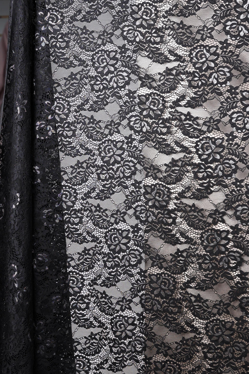 a close-up view of a black and white lace fabric with a floral pattern. The fabric appears to be a sheer lace material, with a black background that contrasts with the white lace. The lace has a delicate and intricate design, with a repeating pattern of flowers and leaves. The fabric is folded and draped, creating a visually appealing and elegant appearance.