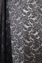 a close-up view of a black and white lace fabric with a floral pattern. The fabric appears to be a sheer lace material, with a black background that contrasts with the white lace. The lace has a delicate and intricate design, with a repeating pattern of flowers and leaves. The fabric is folded and draped, creating a visually appealing and elegant appearance.