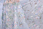 a close-up view of a delicate, intricately embroidered fabric with a floral pattern. The fabric appears to be made of sheer material, allowing the colorful flowers and leaves to be clearly visible. The background is a light blue color, which complements the vibrant colors of the embroidered design. The image does not contain any text or other discernible objects, and the focus is solely on the detailed embroidered pattern.
