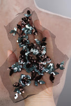A hand holding a piece of fabric with a floral pattern made of sequins and beads.