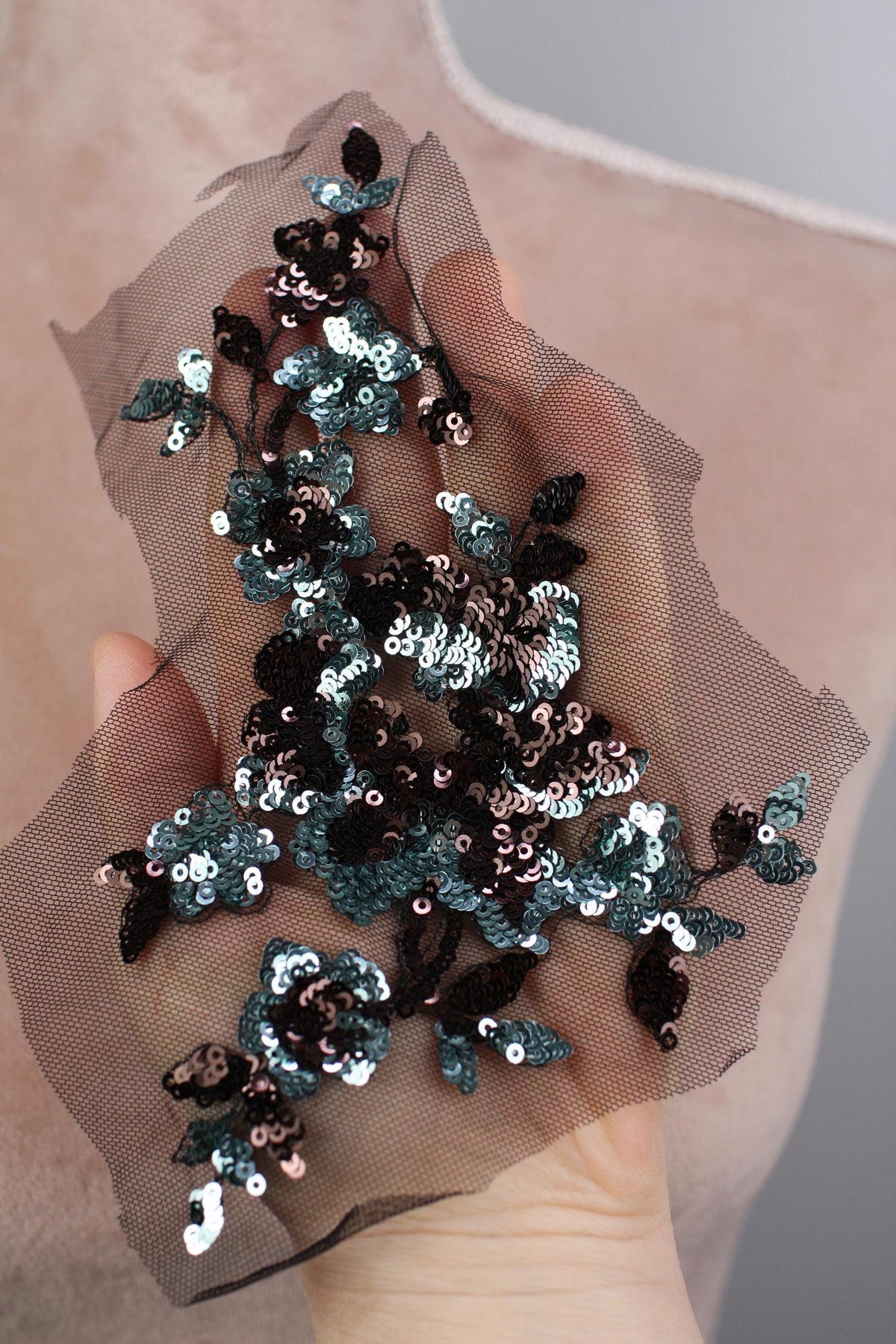 A hand holding a piece of fabric with a floral pattern made of sequins and beads.