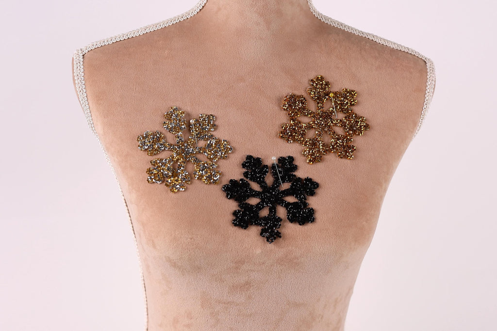 A mannequin torso with three decorative snowflake-shaped embellishments on it, one in gold, one in black, and one in silver.