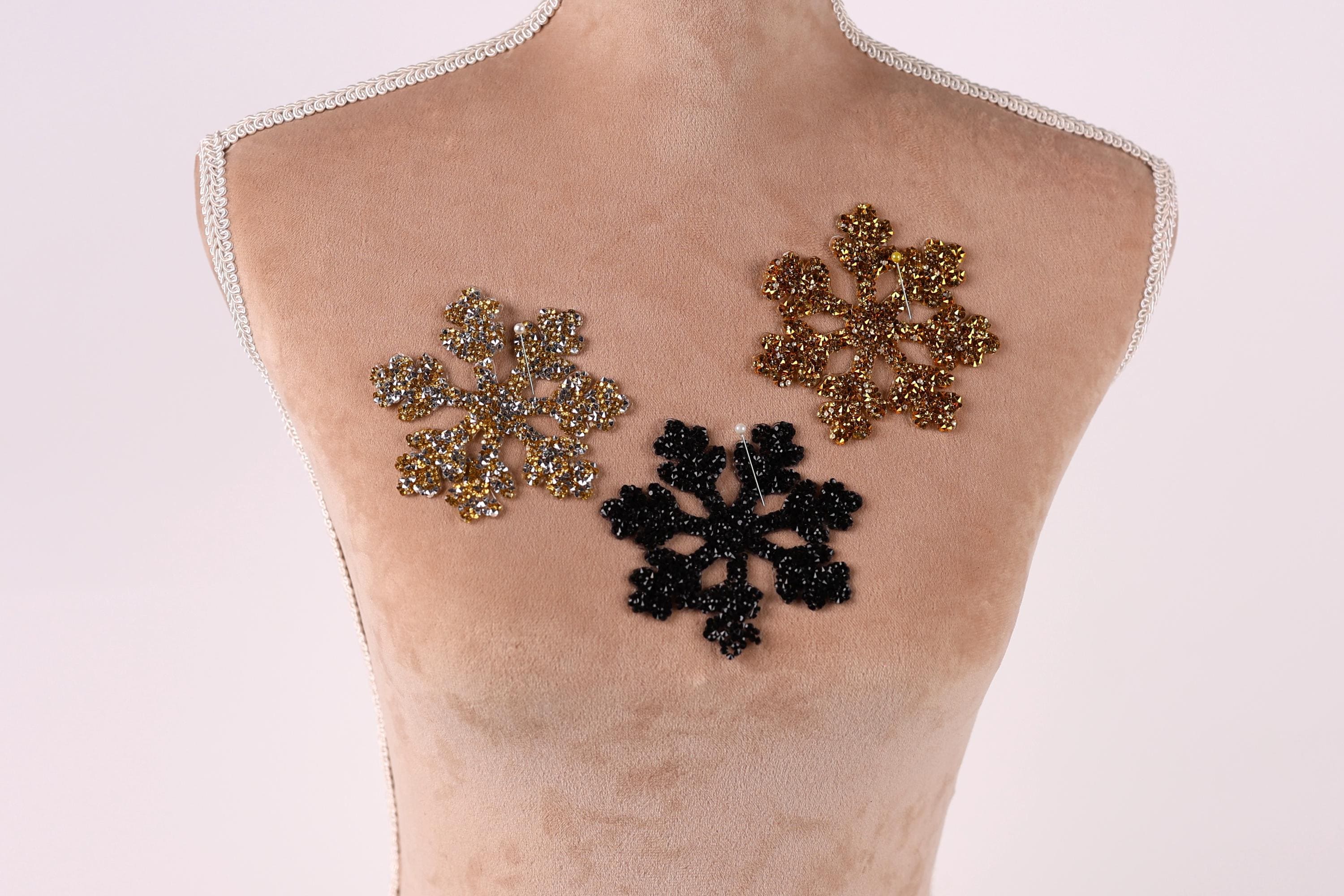 A mannequin torso with three decorative snowflake-shaped embellishments on it, one in gold, one in black, and one in silver.
