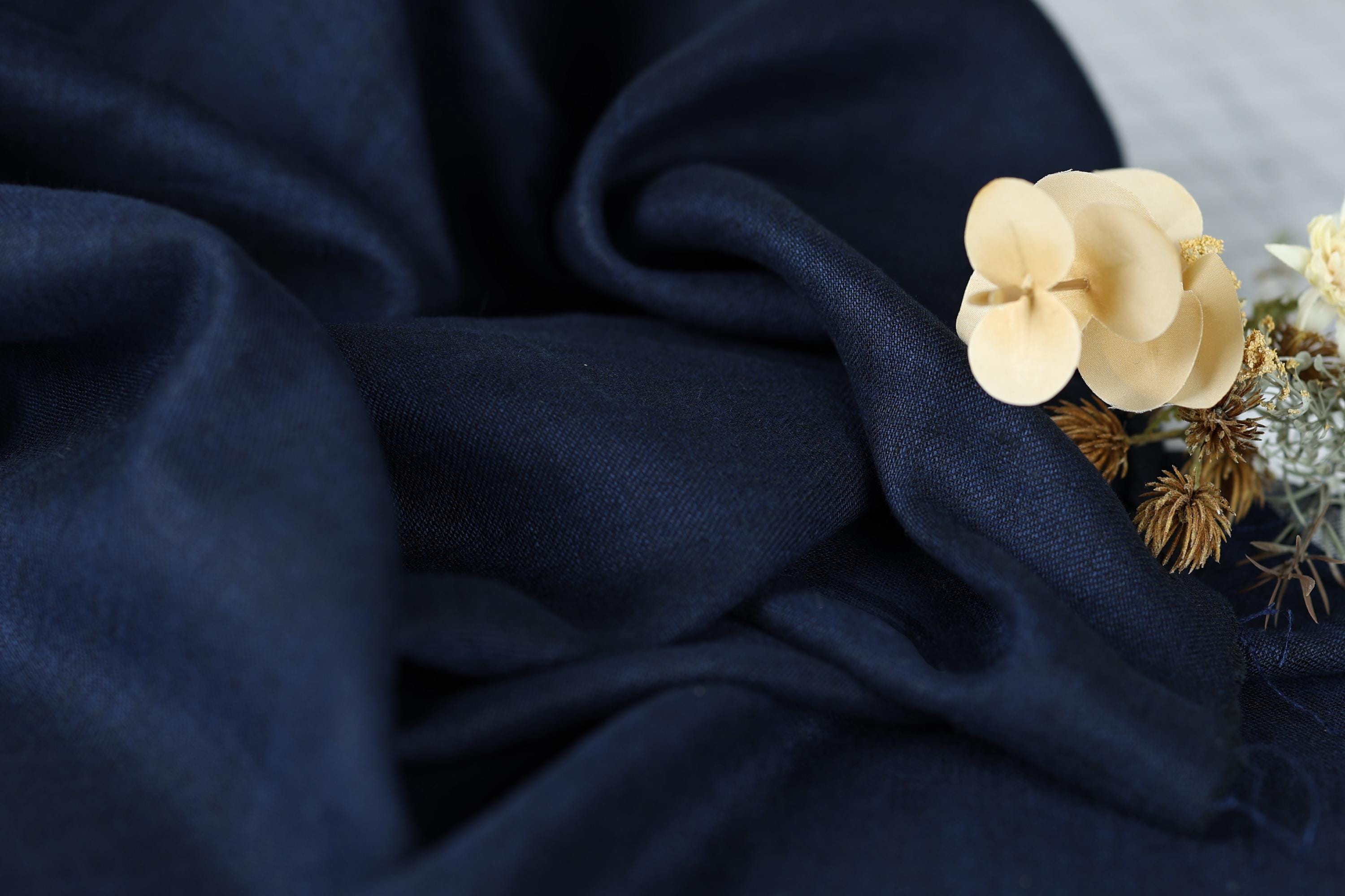 a close-up view of a dark blue fabric with a delicate white flower resting on top of it.