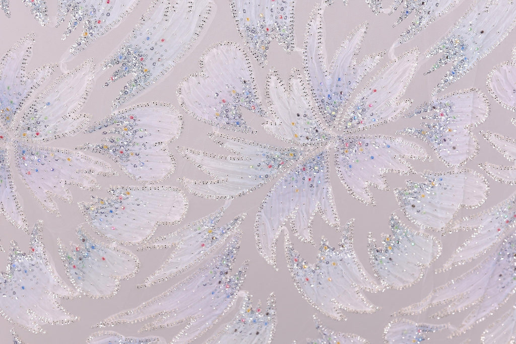 a close-up view of a patterned fabric with a repeating design of white and silver glittering flowers or leaves. The pattern is intricate and detailed, with the glittering elements creating a visually striking contrast against the fabric's texture.