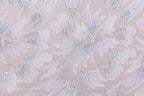 a close-up view of a patterned fabric with a repeating design of white and silver glittering flowers or leaves. The pattern is intricate and detailed, with the glittering elements creating a visually striking contrast against the fabric's texture.