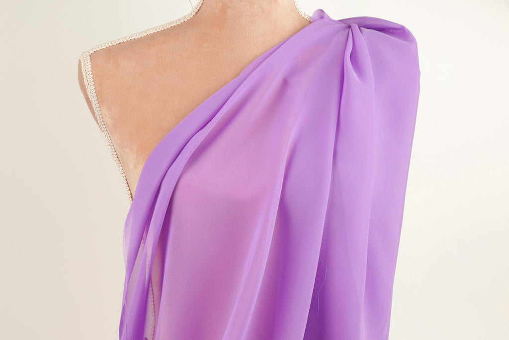A mannequin wearing a purple one-shoulder dress with a draped, flowing fabric.