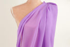 A mannequin wearing a purple one-shoulder dress with a draped, flowing fabric.