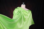 A mannequin wearing a flowing, green satin cape against a dark background.
