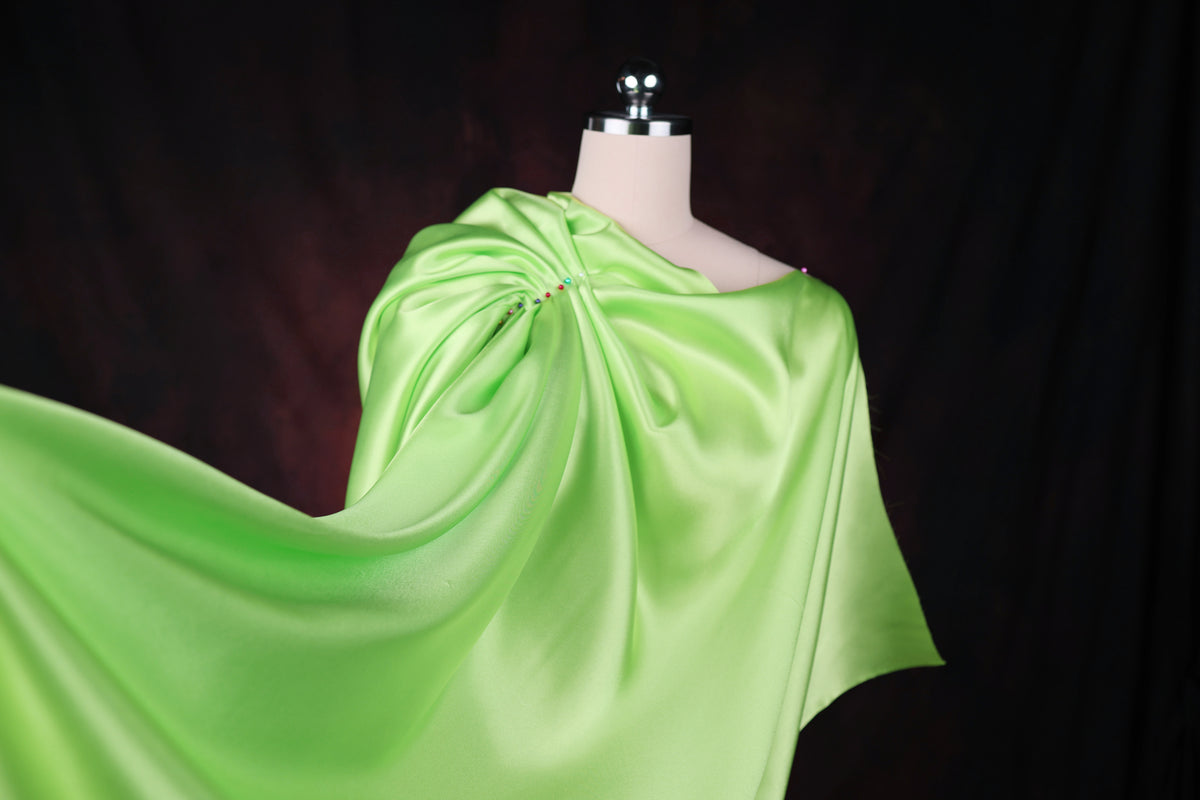 A mannequin wearing a flowing, green satin cape against a dark background.