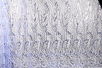 a close-up view of a fabric with a repeating pattern of silver and white leaves or flowers. The pattern is intricate and detailed, creating a visually striking and elegant design.