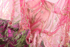 The image is a close-up of a fabric with a pink and green color scheme, adorned with sequins and beads. The fabric appears to be a sheer material, possibly a sheer dress or garment.