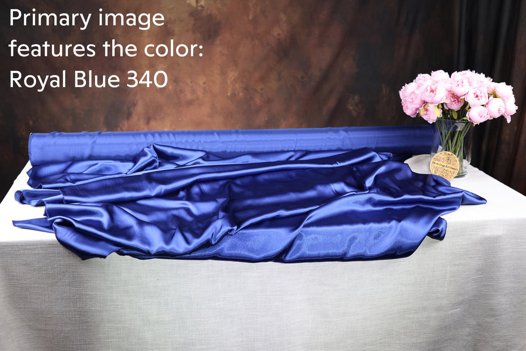 a roll of blue satin fabric and a vase of pink flowers on a table.