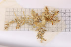 a decorative piece of gold embroidery with a flower and leaves, placed on a ruler for scale.