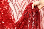 A hand is holding up a red sequin fabric, which appears to be a sheer, sheer fabric with a red and black pattern.