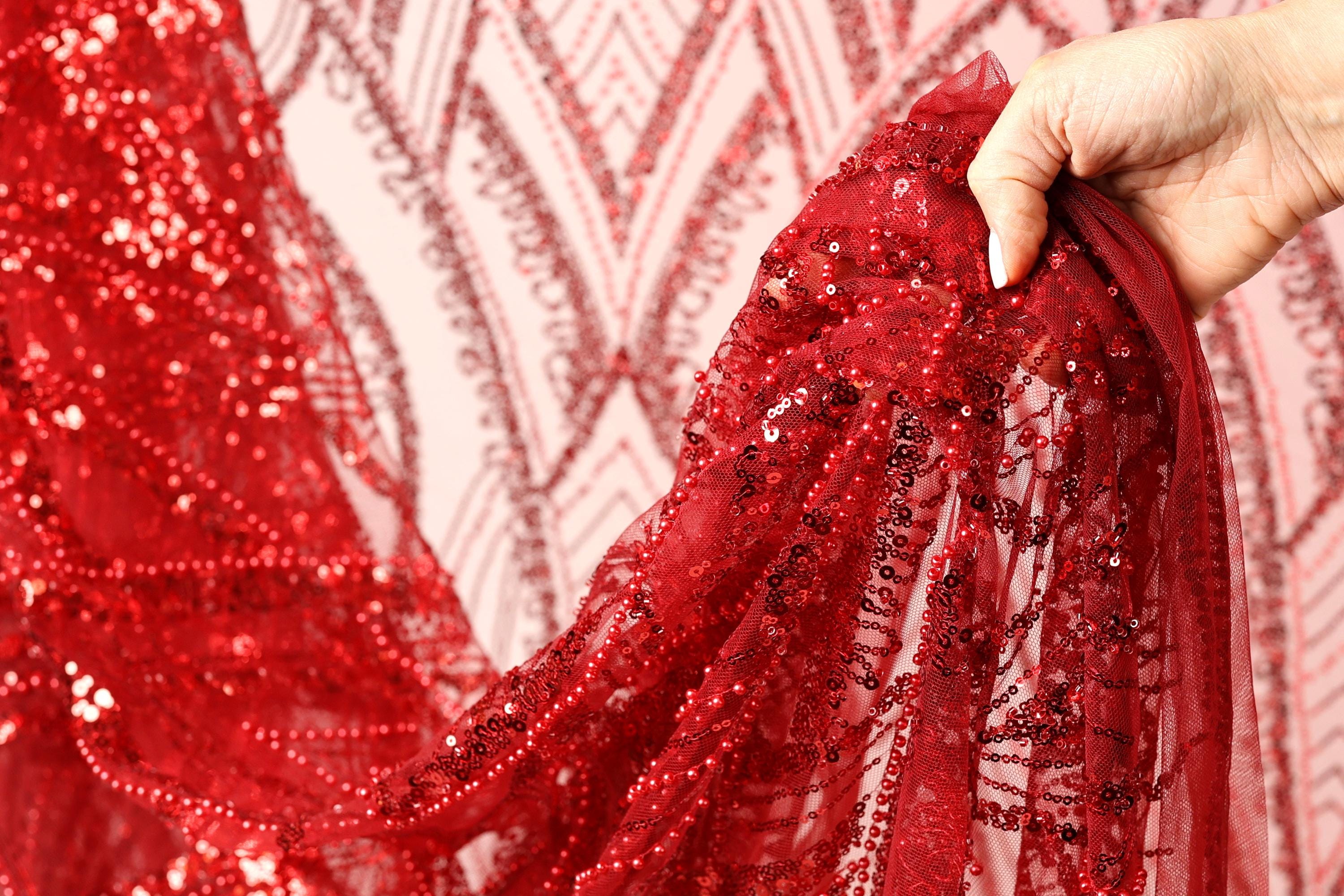 A hand is holding up a red sequin fabric, which appears to be a sheer, sheer fabric with a red and black pattern.