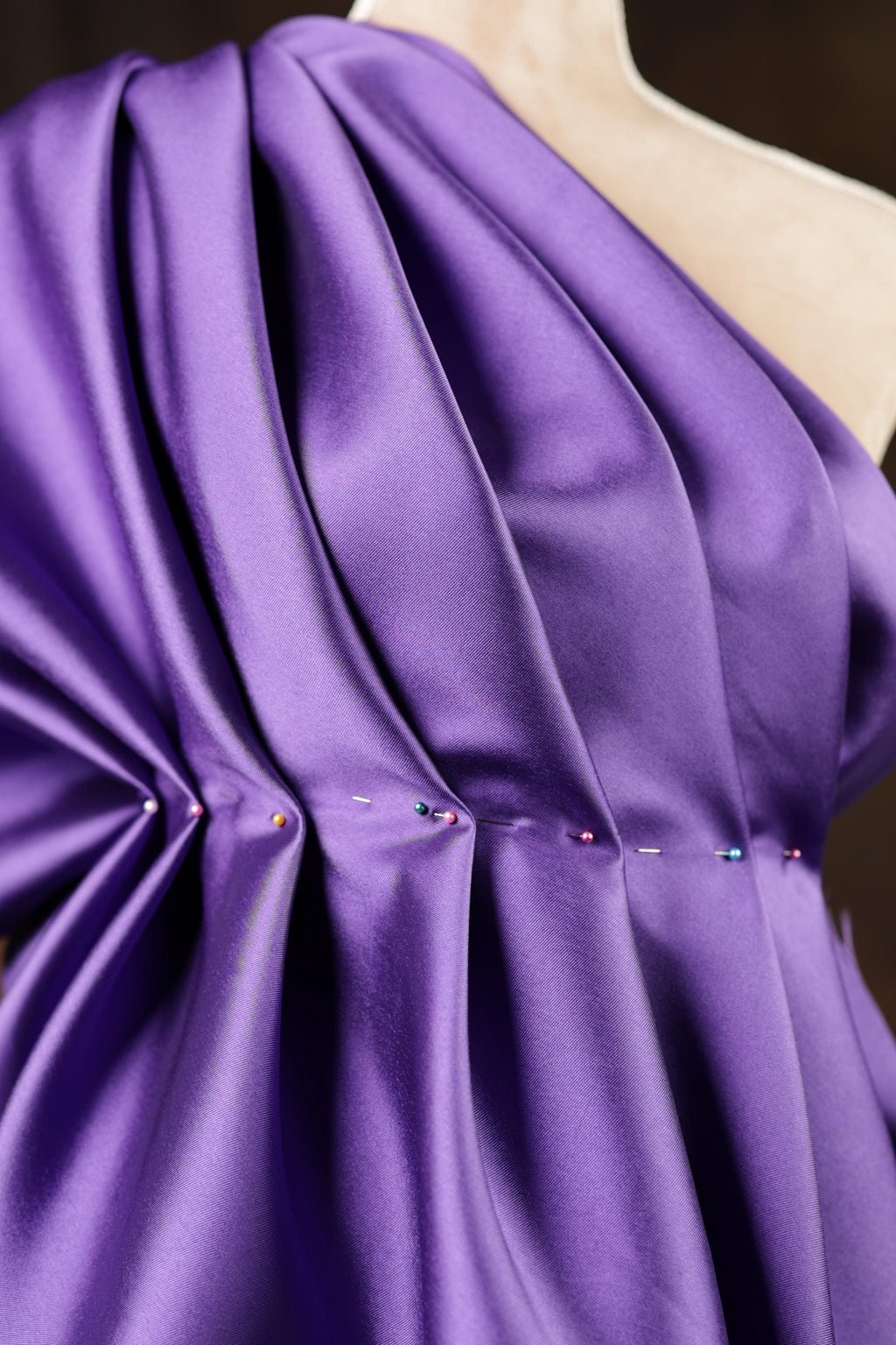 A close-up view of a purple fabric with a ruched design, featuring small pins or needles sewn into the fabric.