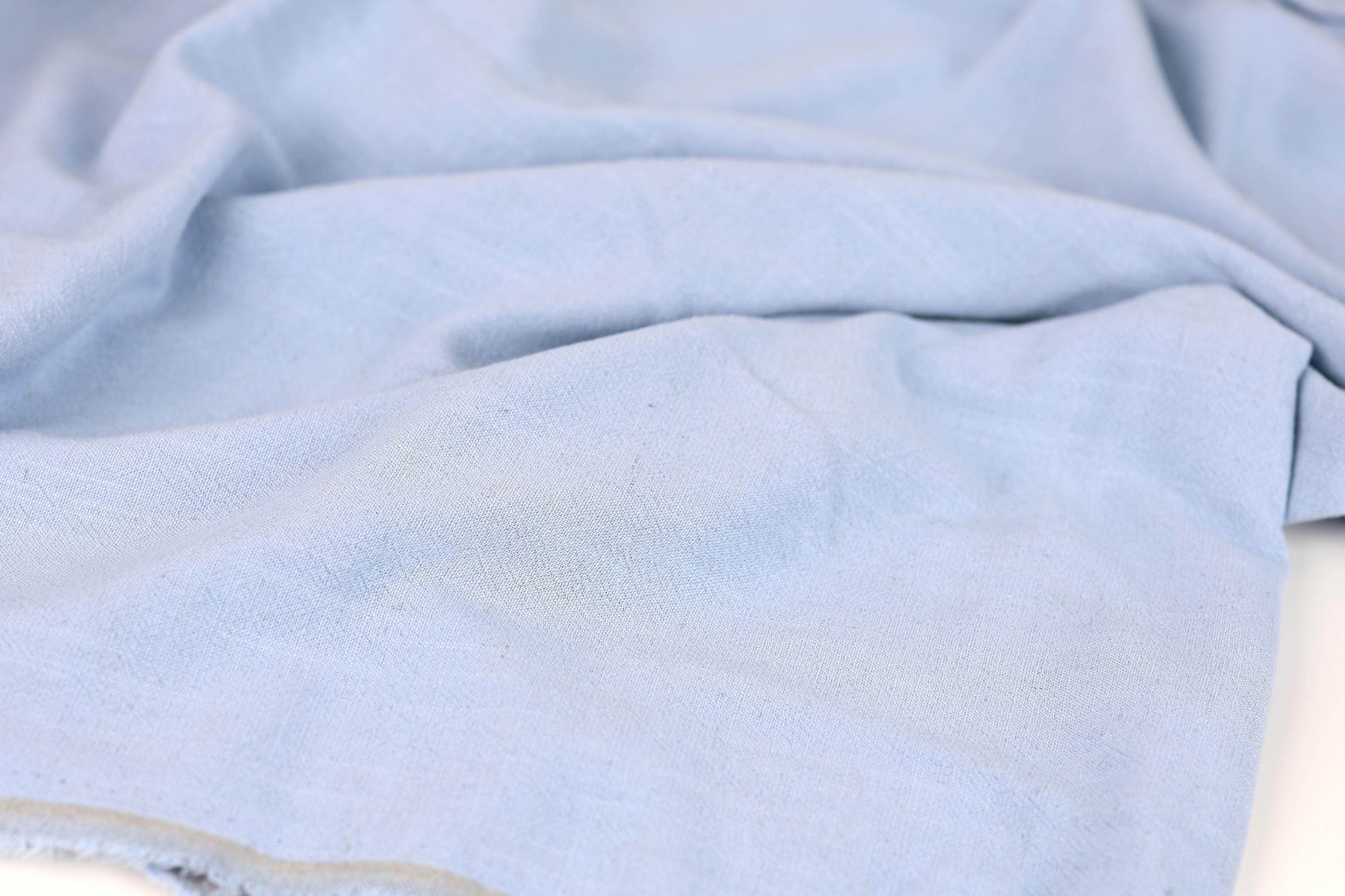 A close-up view of a light blue fabric, possibly cotton or linen, with a slightly wrinkled texture.