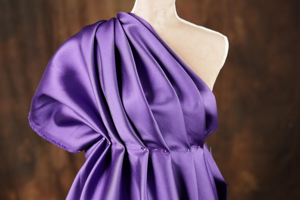 A mannequin wearing a purple satin dress with a draped, flowing silhouette.