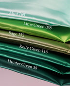 A stack of five fabric swatches in various shades of green, including mint, lime green, sage, Kelly green, and hunter green.