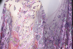 a mannequin wearing a sheer, sequined fabric with a vibrant purple and pink color scheme. The fabric appears to be a sheer, lace-like material with a floral pattern, and it is draped over the mannequin's body. The mannequin is positioned in a way that highlights the intricate details and patterns of the fabric.