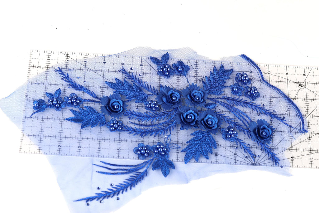 a close-up view of a piece of fabric adorned with blue flowers and leaves, which are meticulously crafted and placed on a transparent ruler for scale.