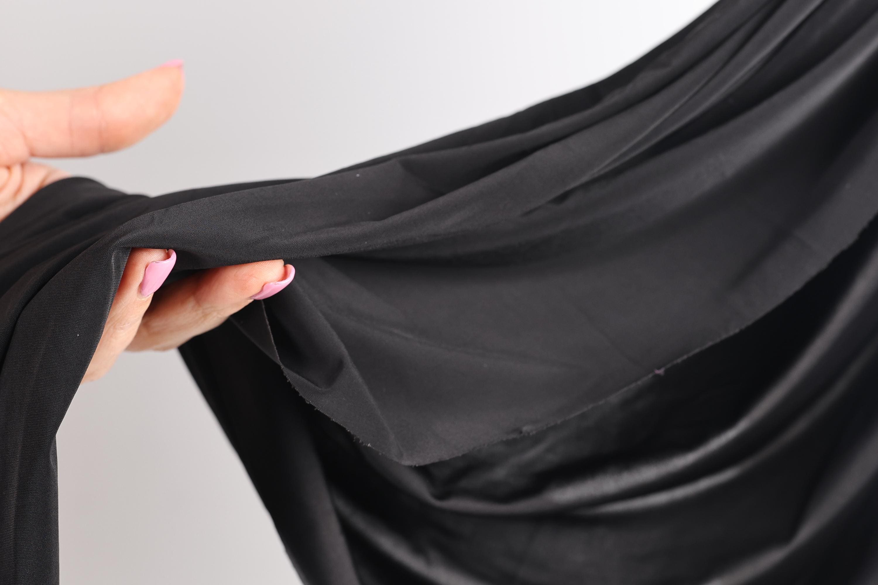 A hand holding a black fabric, with the fingers curled around it.