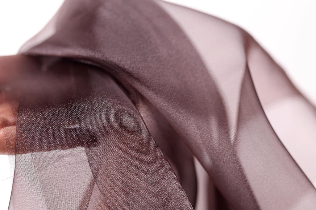 A close-up view of a piece of brown fabric, possibly silk or chiffon, with a blurred background.