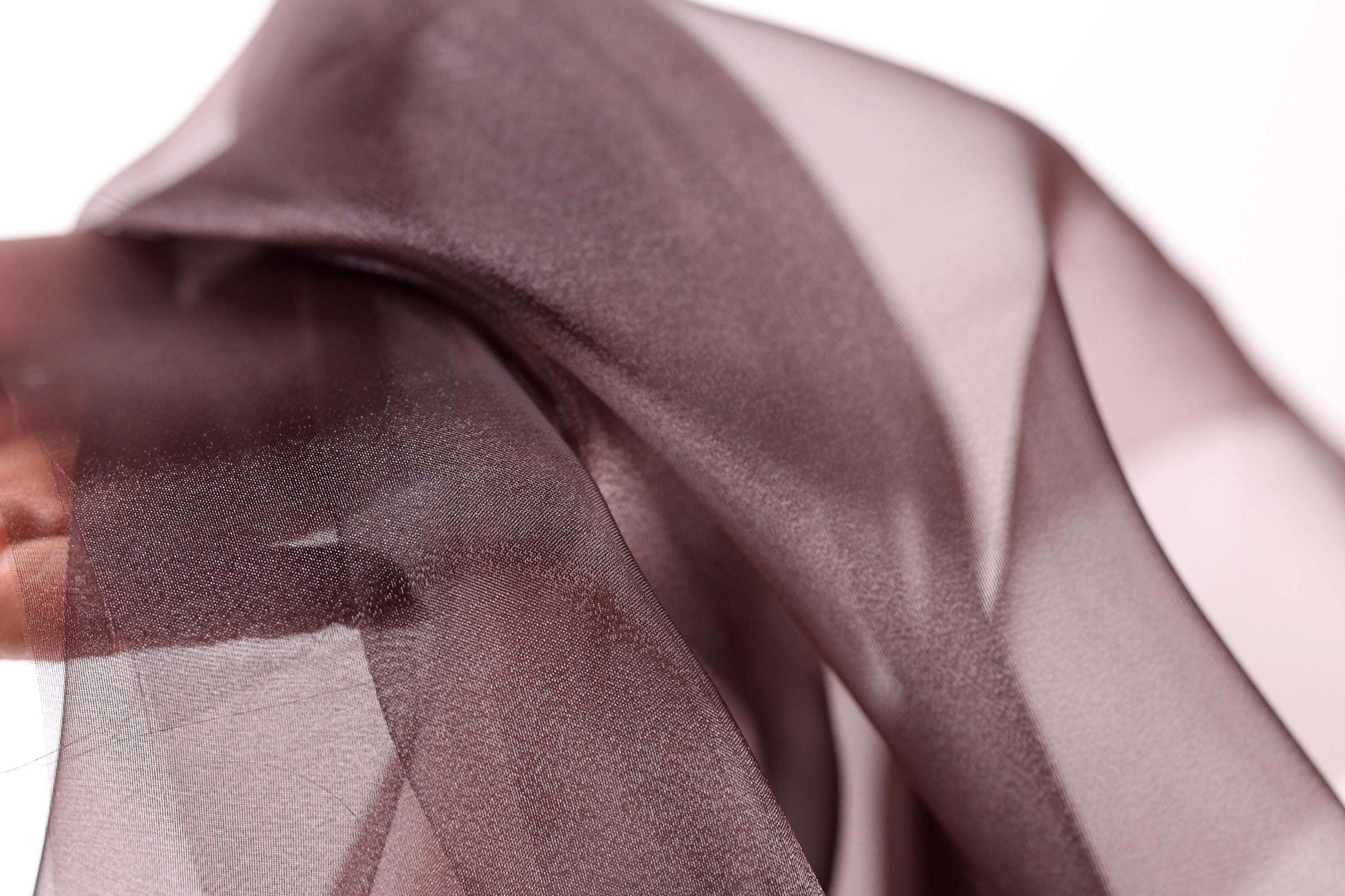 A close-up view of a piece of brown fabric, possibly silk or chiffon, with a blurred background.