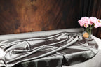 a gray fabric draped over a table, with a vase of pink flowers placed next to it.
