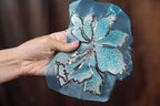 A hand holding a piece of blue fabric with a silver sequin flower design.