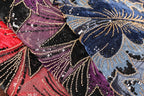 The image is a close-up of a fabric with a vibrant, colorful, and intricate design featuring a variety of sequins and beads in shades of red, blue, and purple.