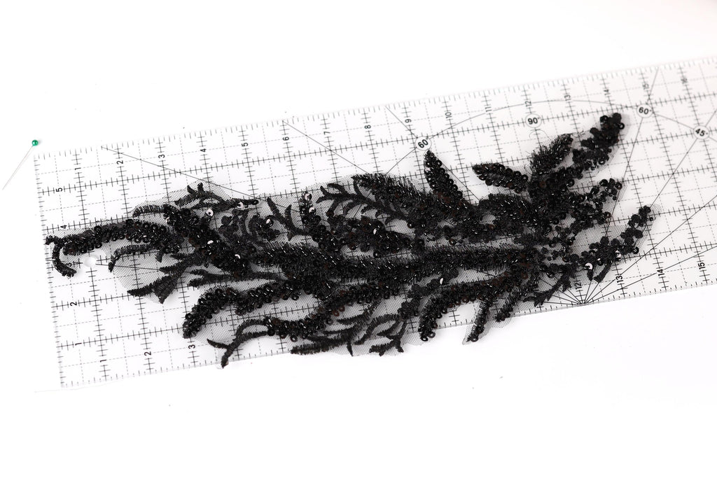 a close-up view of a black lace-like material with a floral pattern, placed on a ruler for scale.