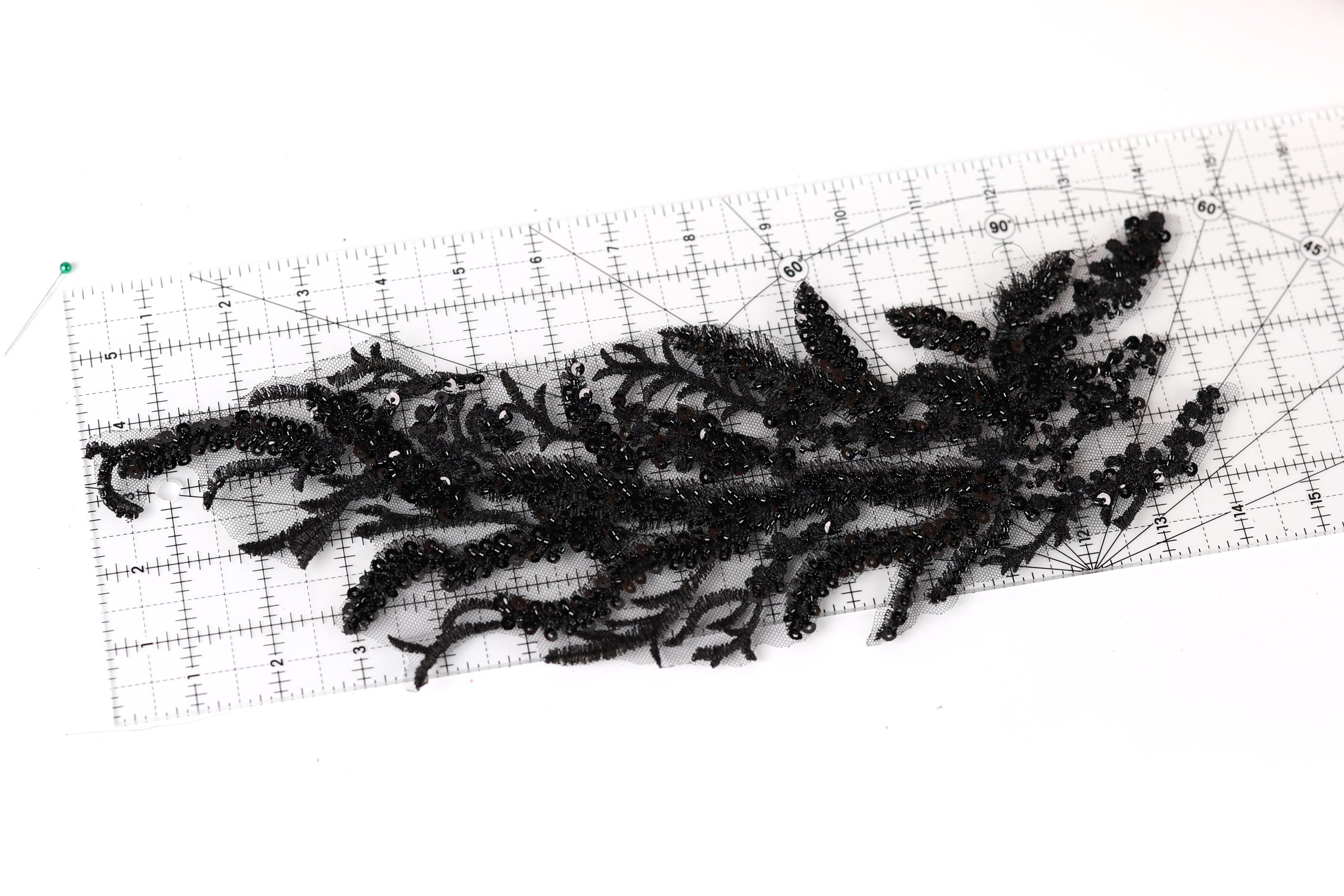 a close-up view of a black lace-like material with a floral pattern, placed on a ruler for scale.